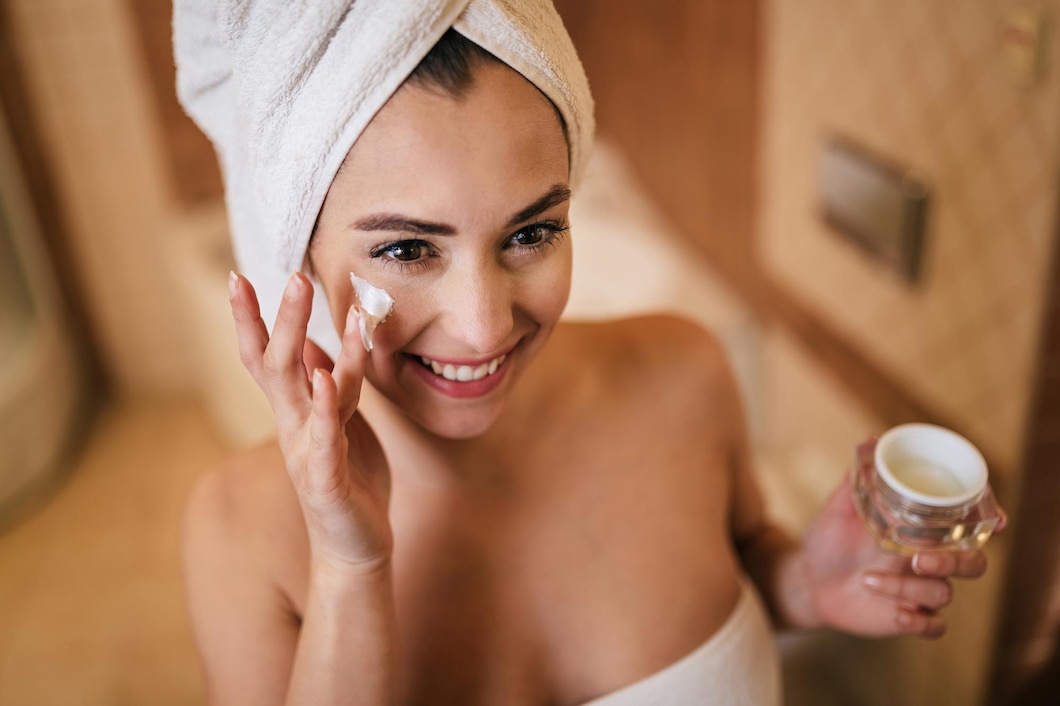 young-beautiful-woman-wrapped-towel-applying-moisturizer-her-face-bathroom_637285-3692